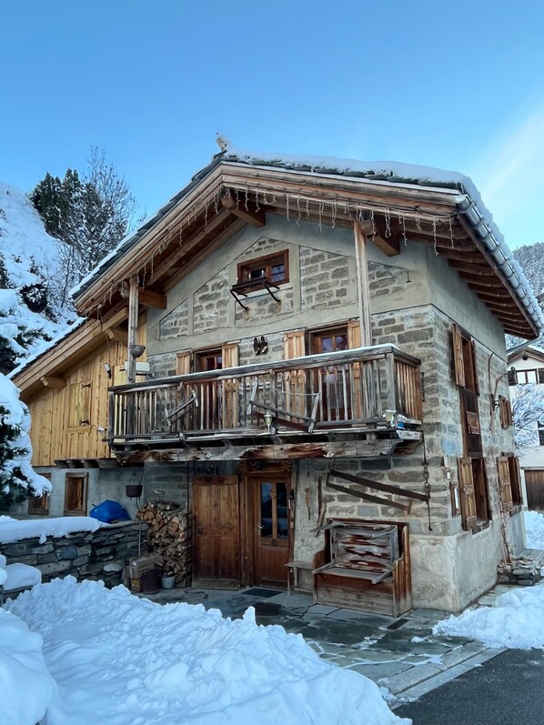 A stone building with a wooden balcony, a wooden door, and a snow-covered landscape.