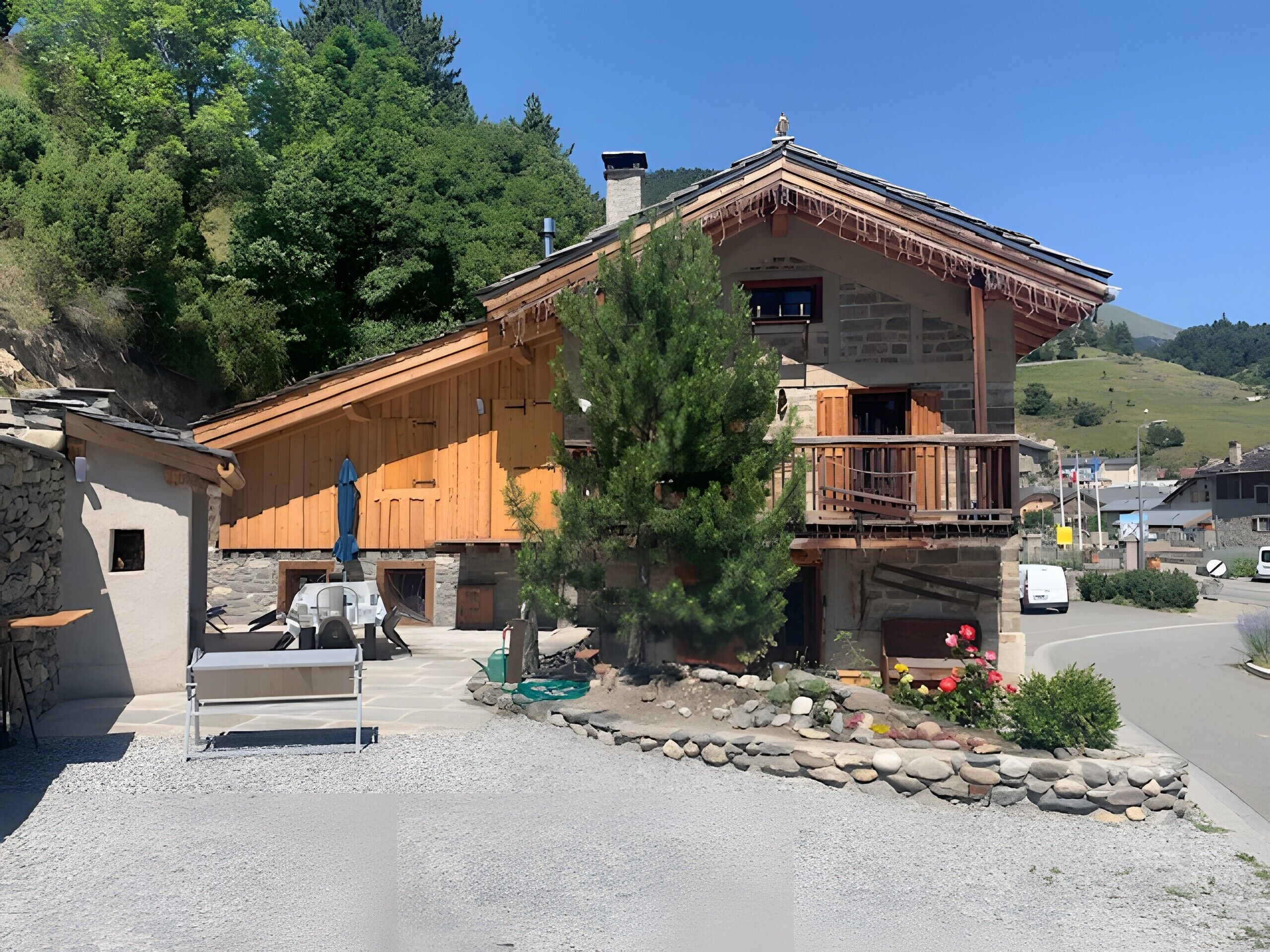 A wooden chalet with a stone foundation, a balcony, and a stone wall.