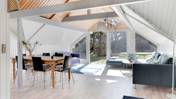 An open-plan living area with a dining table and chairs, a sofa, and a view of the outdoors.