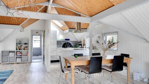 A modern loft with a high ceiling, open kitchen, dining area with chairs, and a visible staircase.