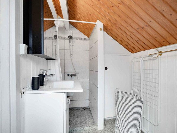 A compact, modern bathroom with a white sink, a shower, and a small storage cabinet.
