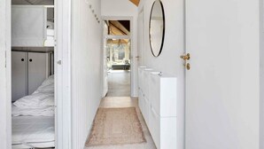 A narrow hallway with a wooden ceiling and white walls, leading to a bathroom with a mirror and a sink.