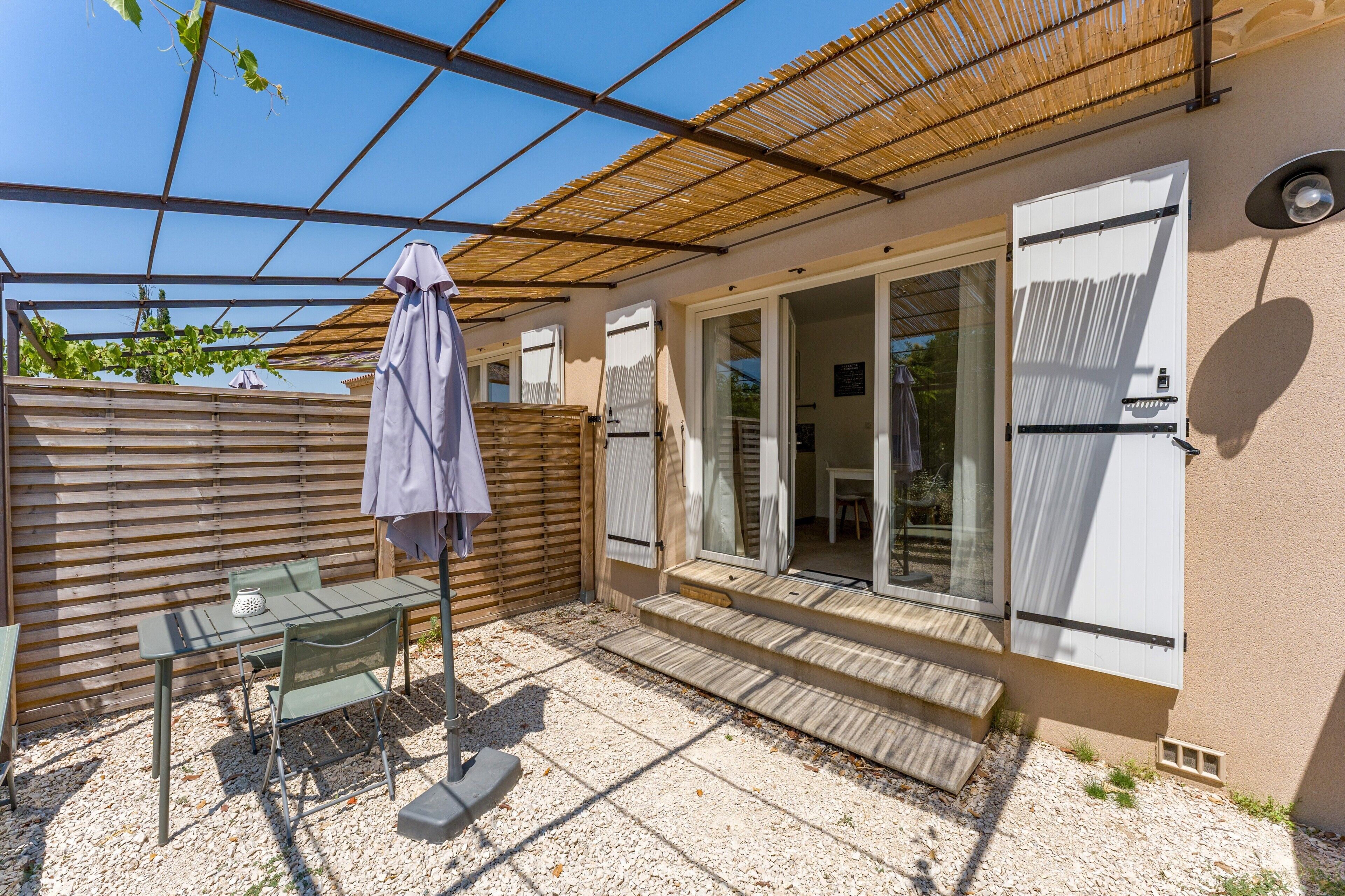 Eine Terrasse mit Tisch und Stühlen, ein überdachter Bereich und eine Glastür zu einem Innenraum.