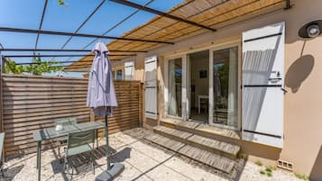 Um pátio com mesa e cadeiras, área coberta e porta de vidro deslizante que dá para um espaço interno.