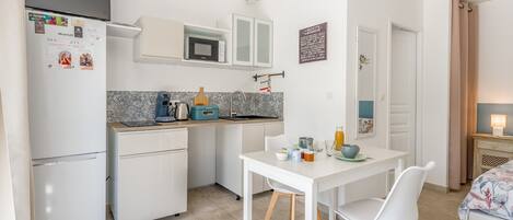 Een compacte keuken met een koelkast, magnetron en een eettafel met stoelen.