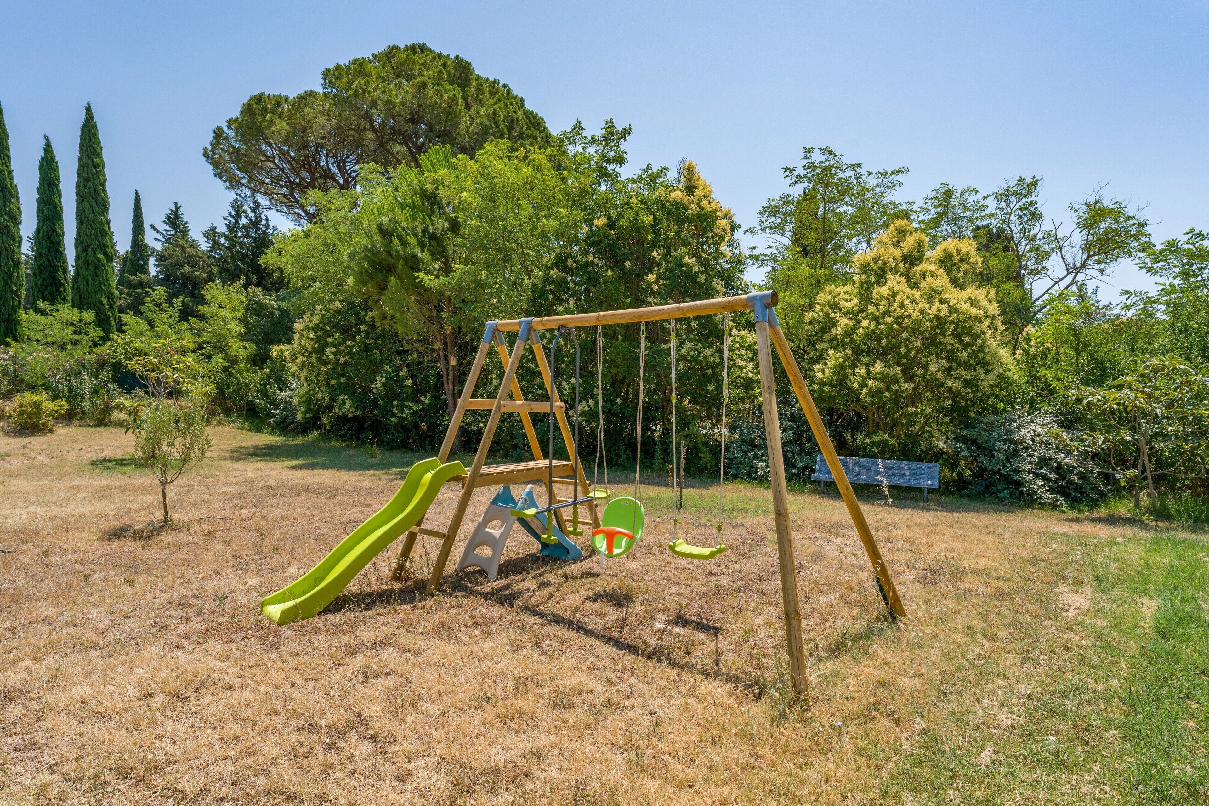 Une balançoire en bois installée dans un espace verdoyant, avec des arbres et un ciel dégagé.