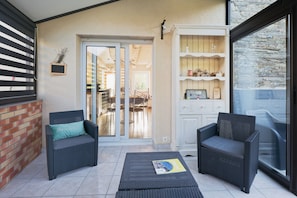 Un patio couvert comprenant deux fauteuils en osier, une petite table et une porte-fenêtre coulissante donnant sur un espace extérieur aménagé pour s’asseoir.