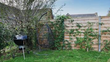 A backyard with a wooden fence, a hanging chair, and a barbecue grill.