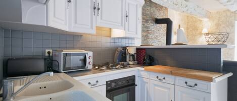 Una cocina con armarios blancos, microondas, estufa y pileta.