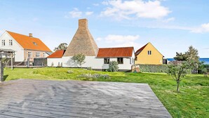 A coastal property with a wooden deck, a large brick chimney, and houses with red roofs. - 5 Star Holiday Home in Svaneke (Svaneke)