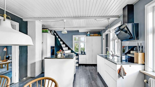 A modern kitchen with white cabinets, a central island, and a staircase leading to another level. - 5 Star Holiday Home in Svaneke (Svaneke)