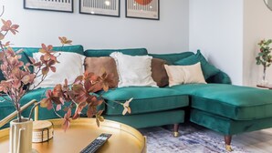 Un sofá verde con varios cojines, un control remoto y plantas decorativas sobre una mesa de madera.