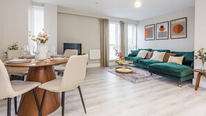 Una sala de estar moderna con comedor, sofá verde y una obra de arte en la pared.