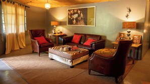 A living room with a brown leather sofa, a matching ottoman, and a wooden coffee table. There is a red throw pillow on the sofa, a lamp on a side table, and a framed picture on the wall.