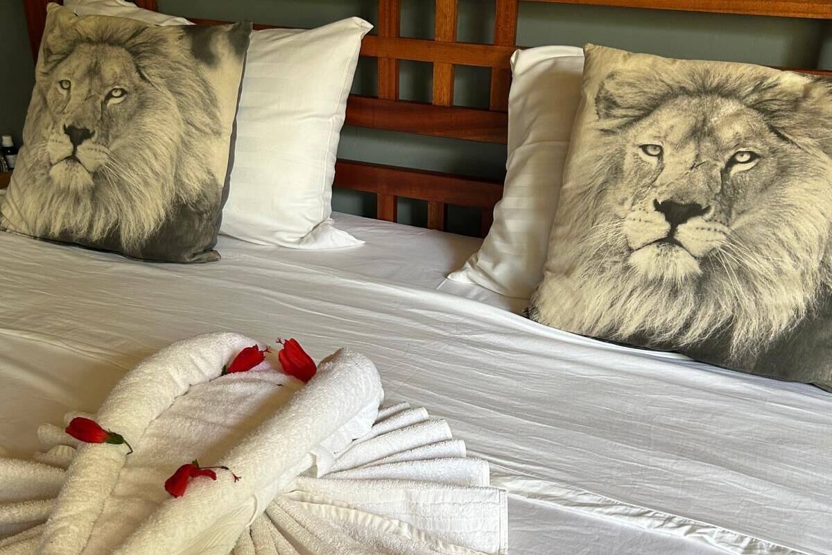 Ein Bett mit einem hölzernen Kopfteil, zwei Kissen mit Löwenmuster und ein Handtuch mit Rosenblütenblättern.