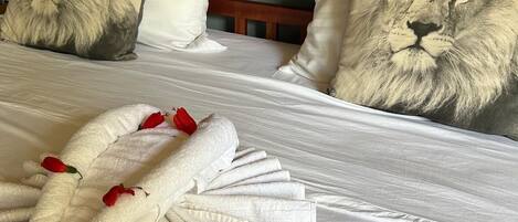A bed with a wooden headboard, two pillows with lion prints, and a towel with rose petals.