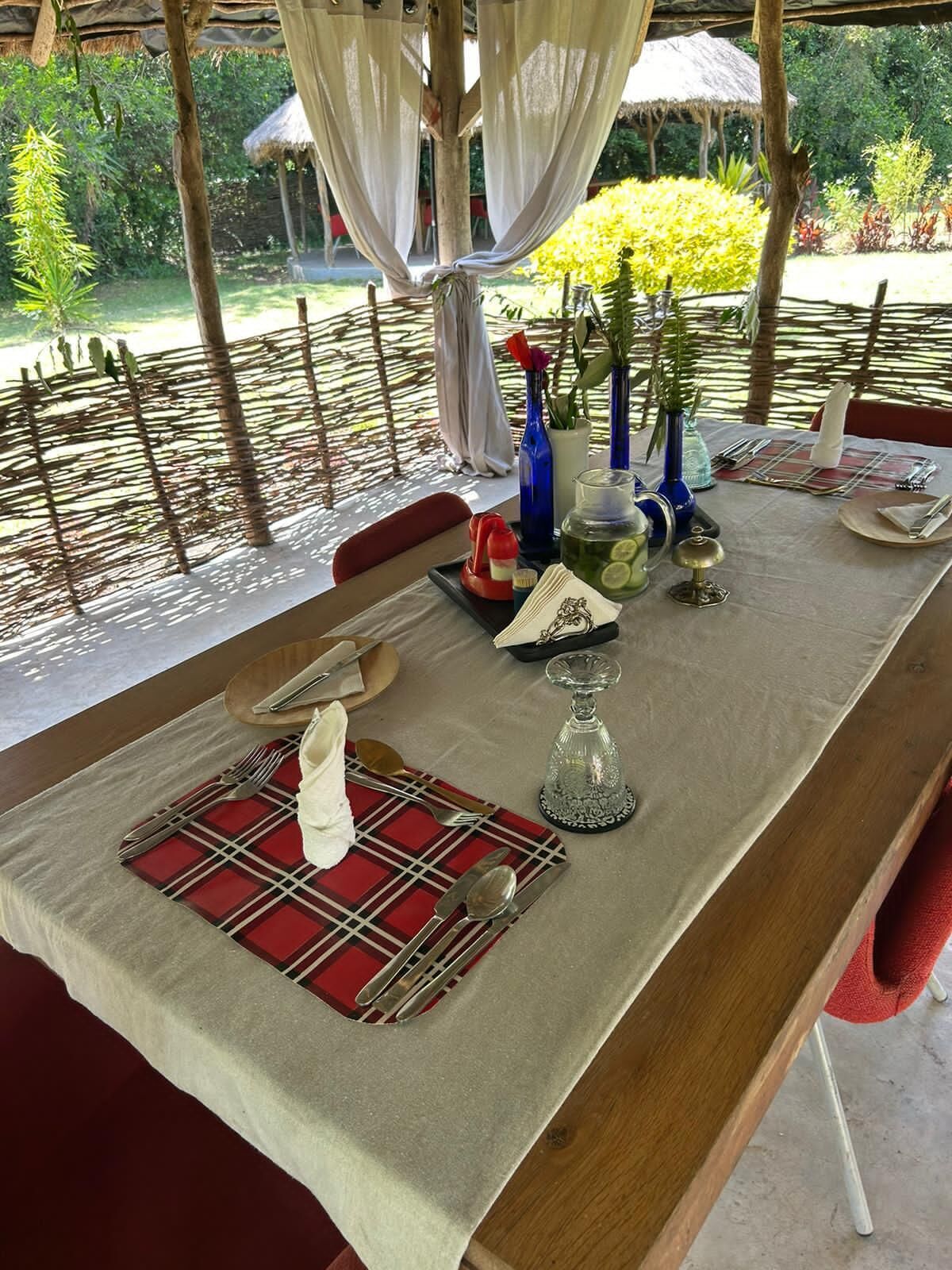 A dining table set with a red and white checkered placemat, silverware, a glass pitcher, and decorative vases.