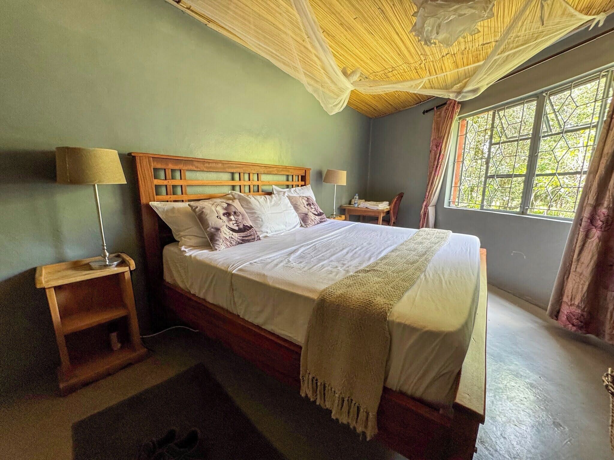 A bed with a wooden headboard, two bedside tables with lamps, a window with curtains, and a woven ceiling.