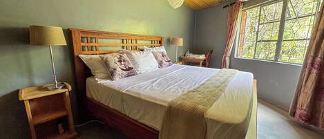A bed with a wooden headboard, two bedside tables with lamps, a window with curtains, and a woven ceiling.