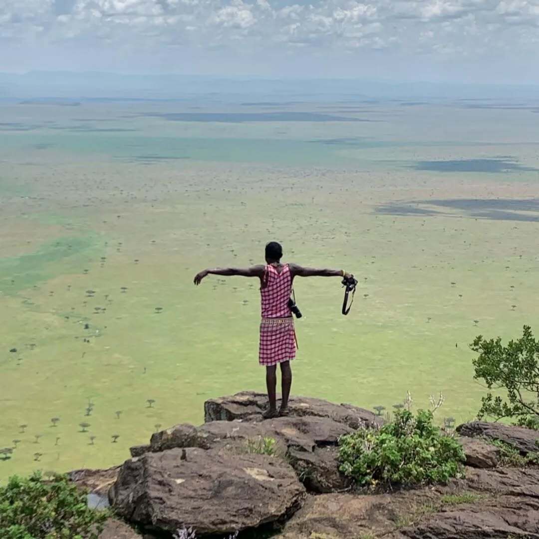A person standing on a rock with arms outstretched, overlooking a vast landscape.