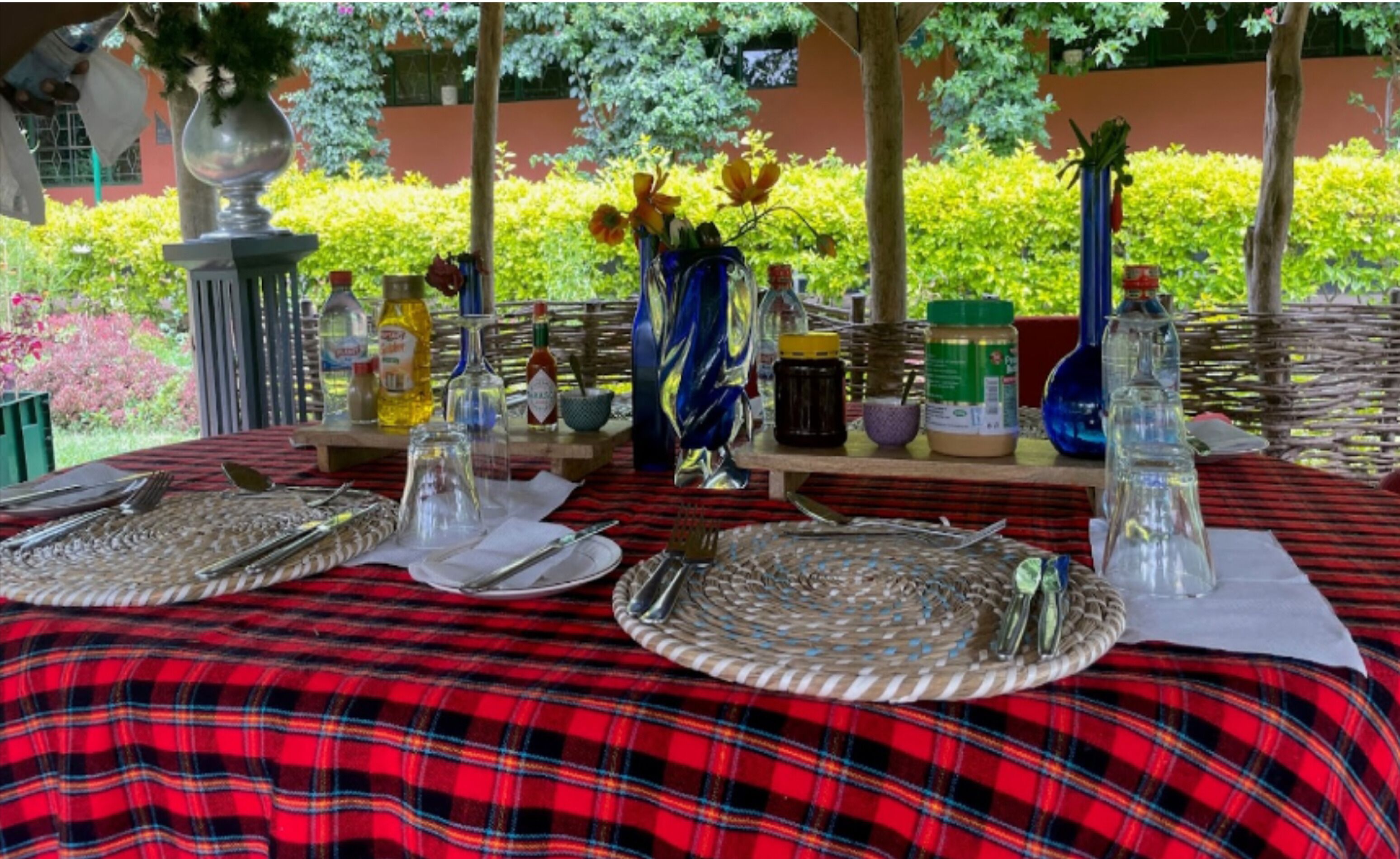 Une table dressée à l’extérieur, recouverte d’une nappe à carreaux rouges et noirs, avec divers condiments et un vase rempli de fleurs.