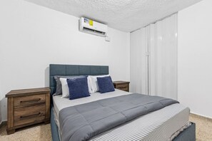 Ein Schlafzimmer mit einem Bett, zwei Nachttischen, einer Wand-Klimaanlage und einem Schiebetürenschrank.