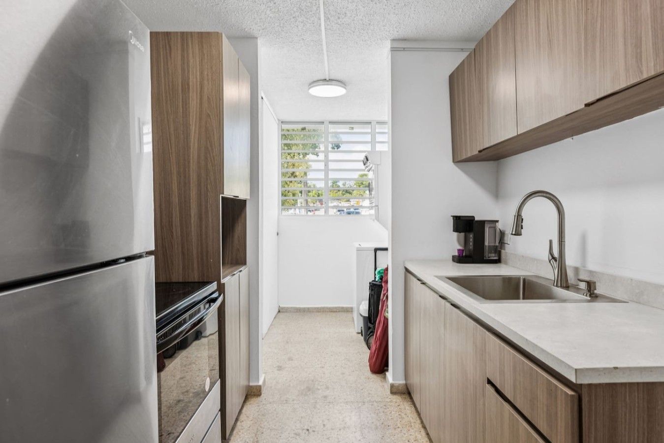 Moderni keittiö, jossa on ruostumattomasta teräksestä valmistetut kodinkoneet, puukaapit ja ikkuna, josta tulee luonnonvaloa.