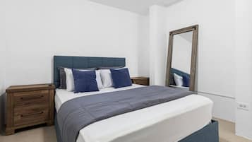 Een slaapkamer met een bed, een houten nachtkastje, een spiegel en een witte muur.