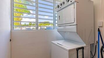 A laundry room with a washing machine and dryer, a window with blinds, and a hose connected to the dryer.