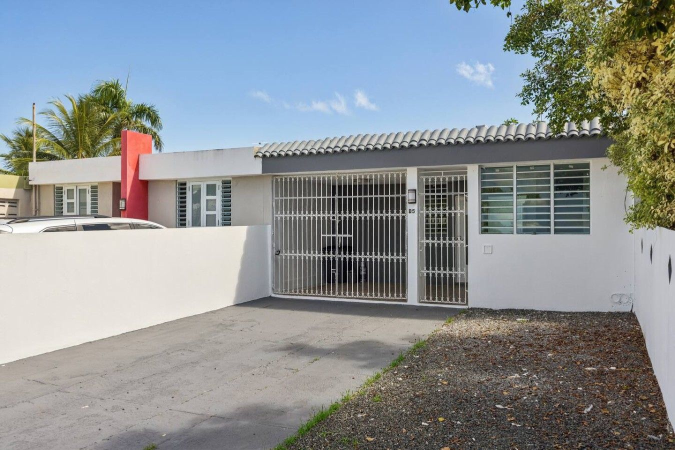 A modern building with a gated entrance, a red accent wall, and a paved driveway.