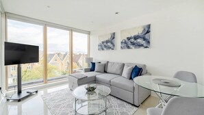 Un salon moderne avec un canapé gris, une table basse en verre et un téléviseur posé sur un meuble.
