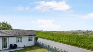 A white house with a grey roof, a paved driveway, and a grassy field in the background. - 5 Star Holiday Home in Dannemare (Dannemare)