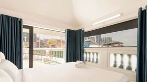 A hotel room with a large bed, a balcony with a view of the city, and a dining area with orange chairs. - Lux white villa 9 Bedrooms (Ho Chi Minh City)