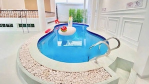 An indoor swimming pool with a central island, clear blue water, and a surrounding pebble bed. - Lux white villa 9 Bedrooms (Ho Chi Minh City)