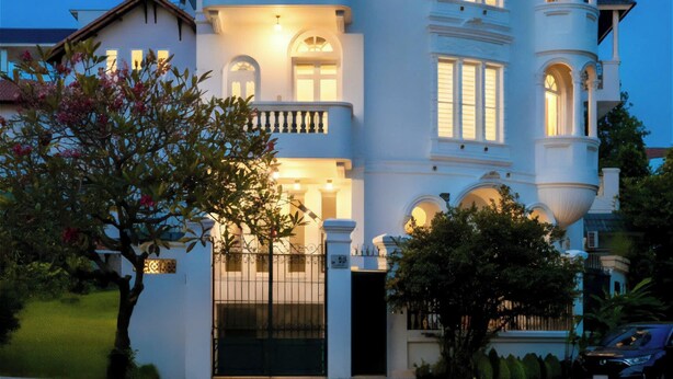 A multi-story building with a balcony, a gated entrance, and string lights. - Lux white villa 9 Bedrooms (Ho Chi Minh City)