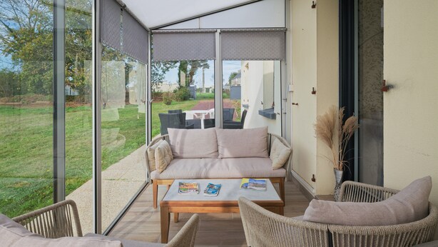 A covered patio with a sofa, chairs, and a table with books. - Les Gîtes de la Morinière - Brocéliande: The Little House on the Prairie (Neant sur Yvel)