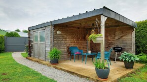 A wooden cabin with a covered porch, two chairs, a table, and potted plants.