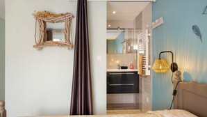 A bedroom with a bed, a nightstand, a wall-mounted lamp, and a bathroom visible through a glass partition.