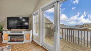 A balcony with a wooden deck, a television on a wooden stand, and a fireplace.