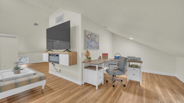 A modern loft bedroom with a large bed, a desk, and a TV mounted on the wall.