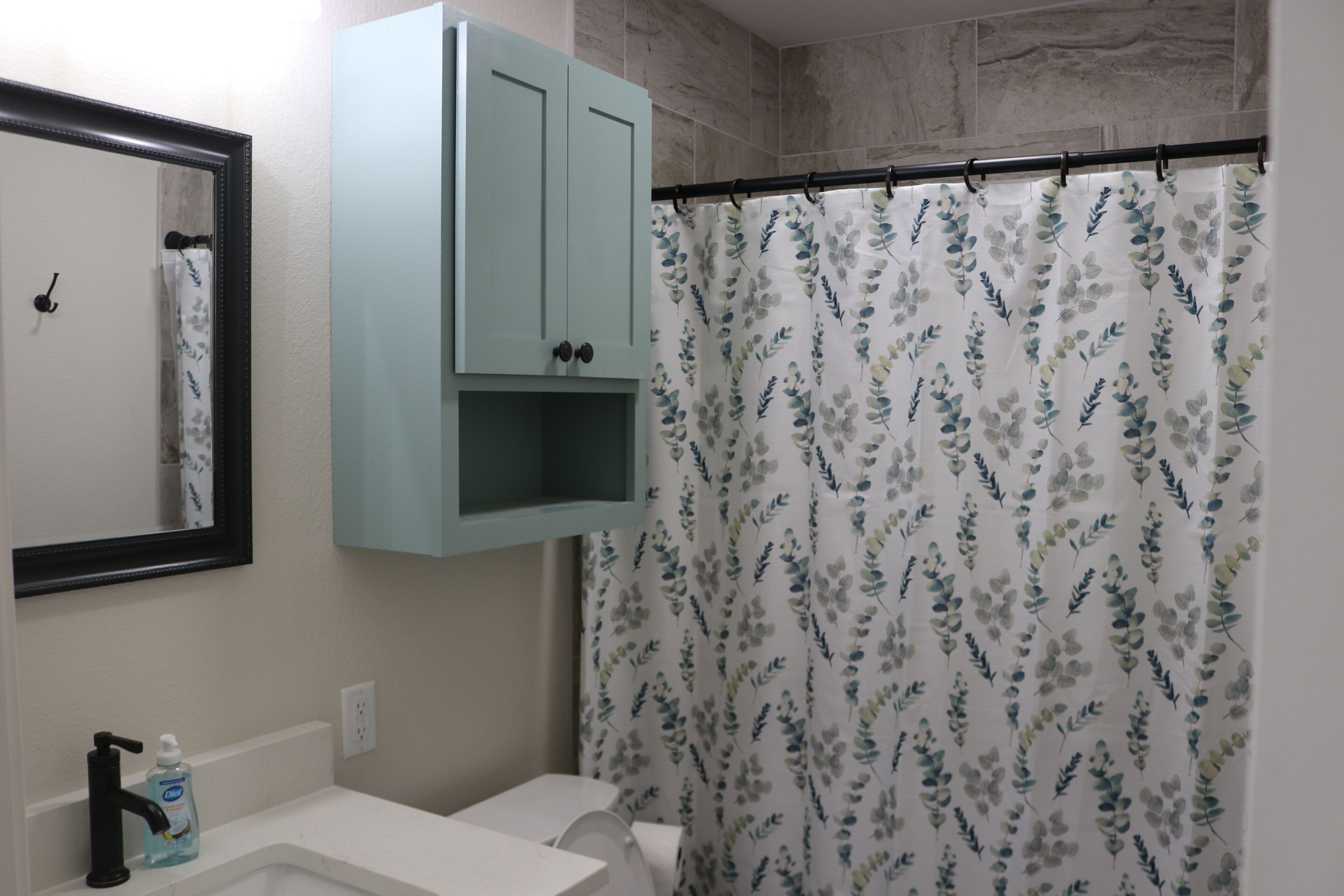 A bathroom with a white sink, a mirror, a light blue cabinet, and a floral shower curtain.