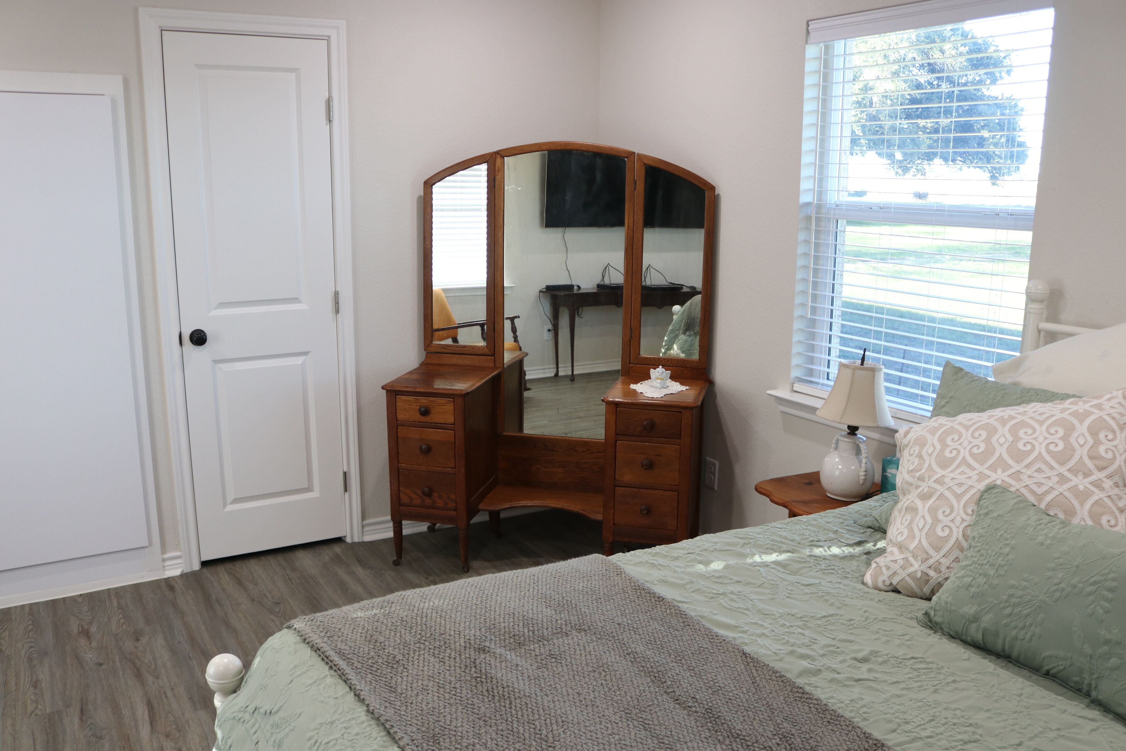 A bedroom with a bed, a dresser, a mirror, a window, and a door.