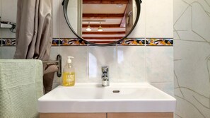 Een badkamer met een witte wastafel, een spiegel, een zeepfles en een handdoekhouder.