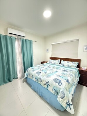 A bedroom with a bed, curtains, an air conditioning unit, a bedside table, and a wall clock. - Marvelous apartment with AC in Oranjestad (Oranjestad)