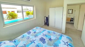 Une chambre à coucher comprenant un lit, une fenêtre donnant sur une piscine, une armoire et une salle de bain.