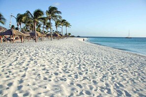 A sandy beach with palm trees and thatched-roof huts. - Charming 1-bedroom apartment in marvelous Oranjestad (Oranjestad)