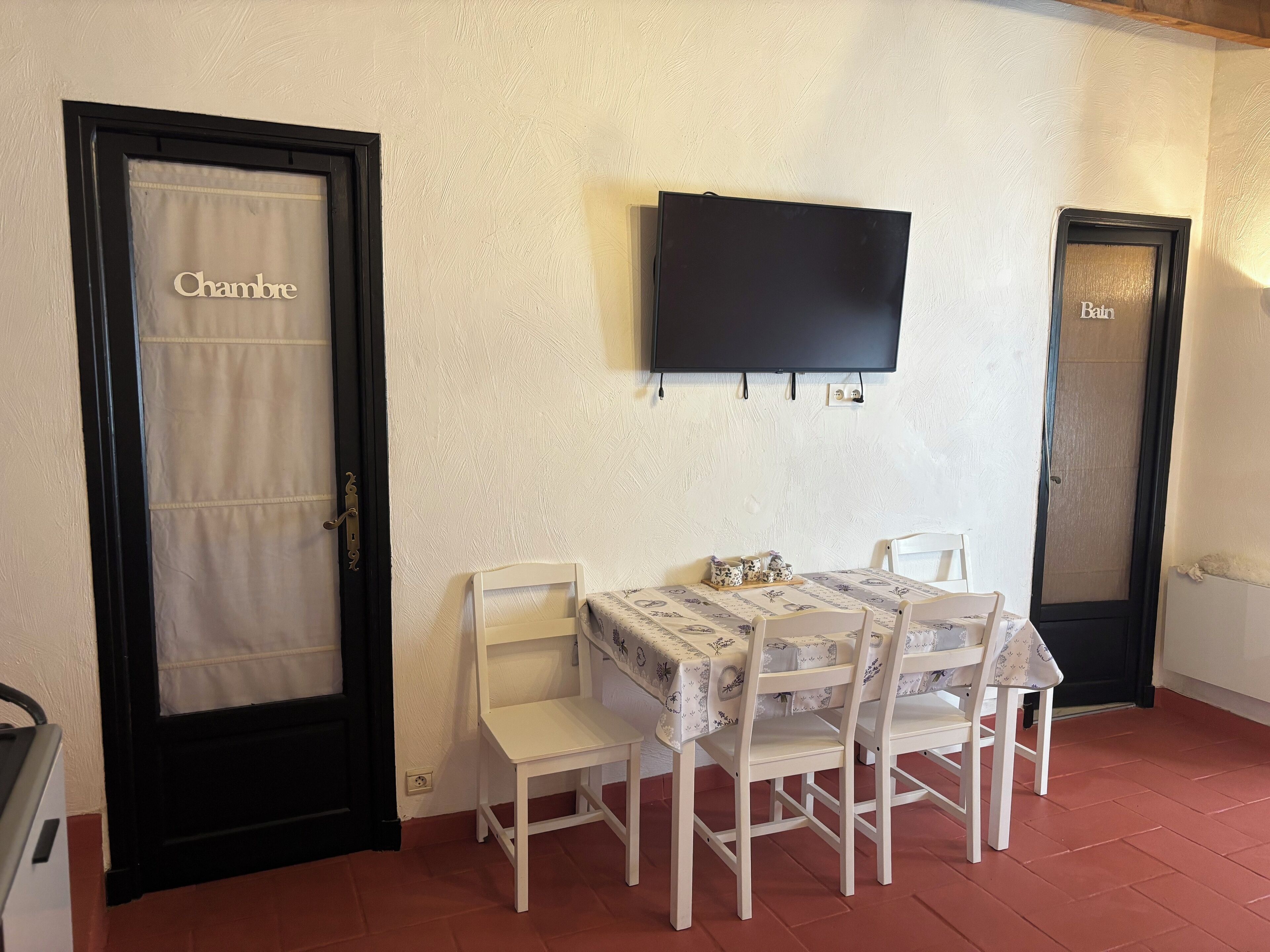 A dining area with a table and chairs, a television mounted on the wall, and two doors labeled "Chambre" and "Bain".