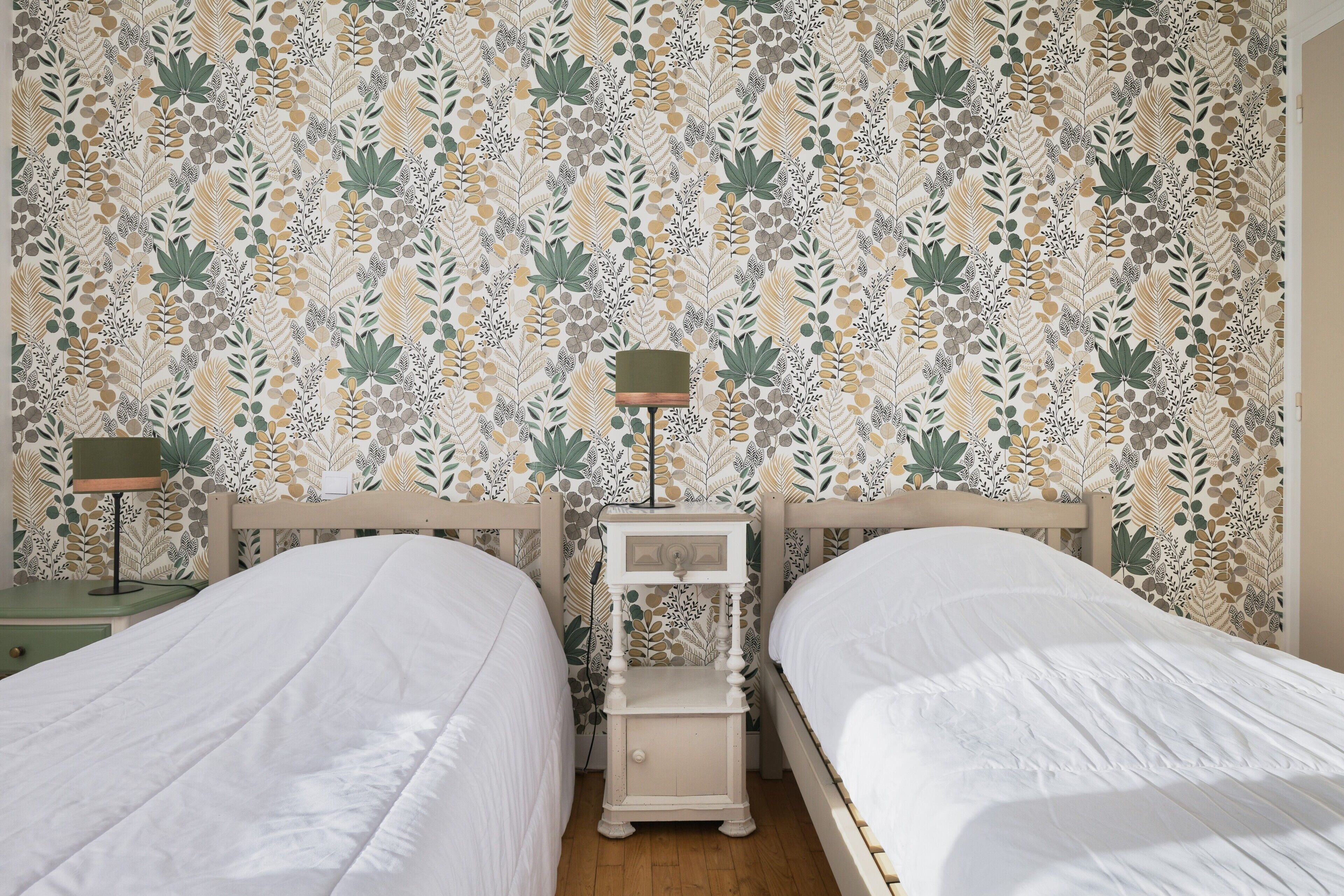 Une chambre avec deux lits, une table de chevet avec une lampe et un papier peint à motifs.