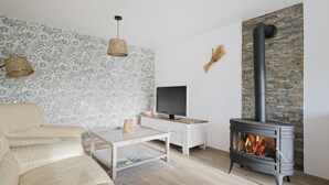 Ett vardagsrum med en soffa, ett soffbord, en tv och en vedkamin.