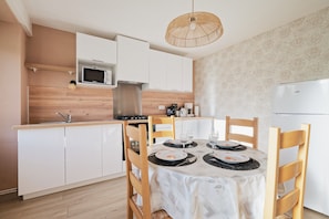 A modern kitchen with white cabinets, a microwave, a stove, and a dining table set for four. - Holiday Home “La Clairière de Merlin” with Private Terrace, Garden and Wi-Fi (Neant sur yvel)